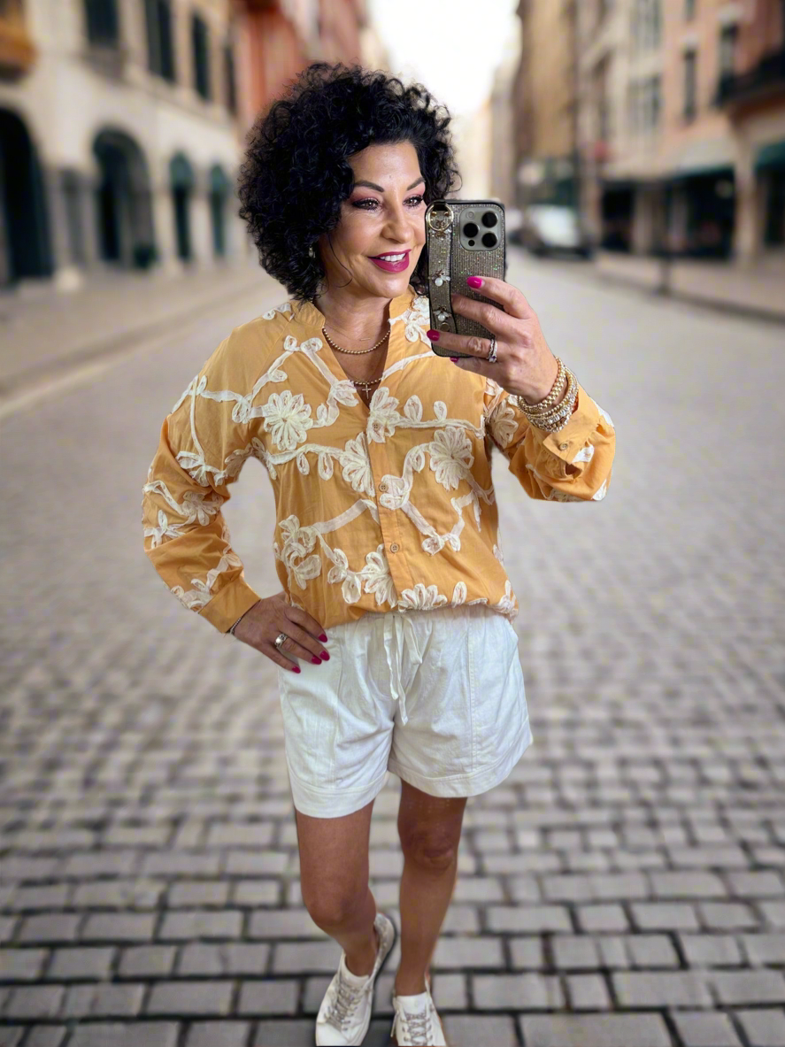 Button cuff closure long sleeve top featuring floral applique all over. Accented wood front button closure